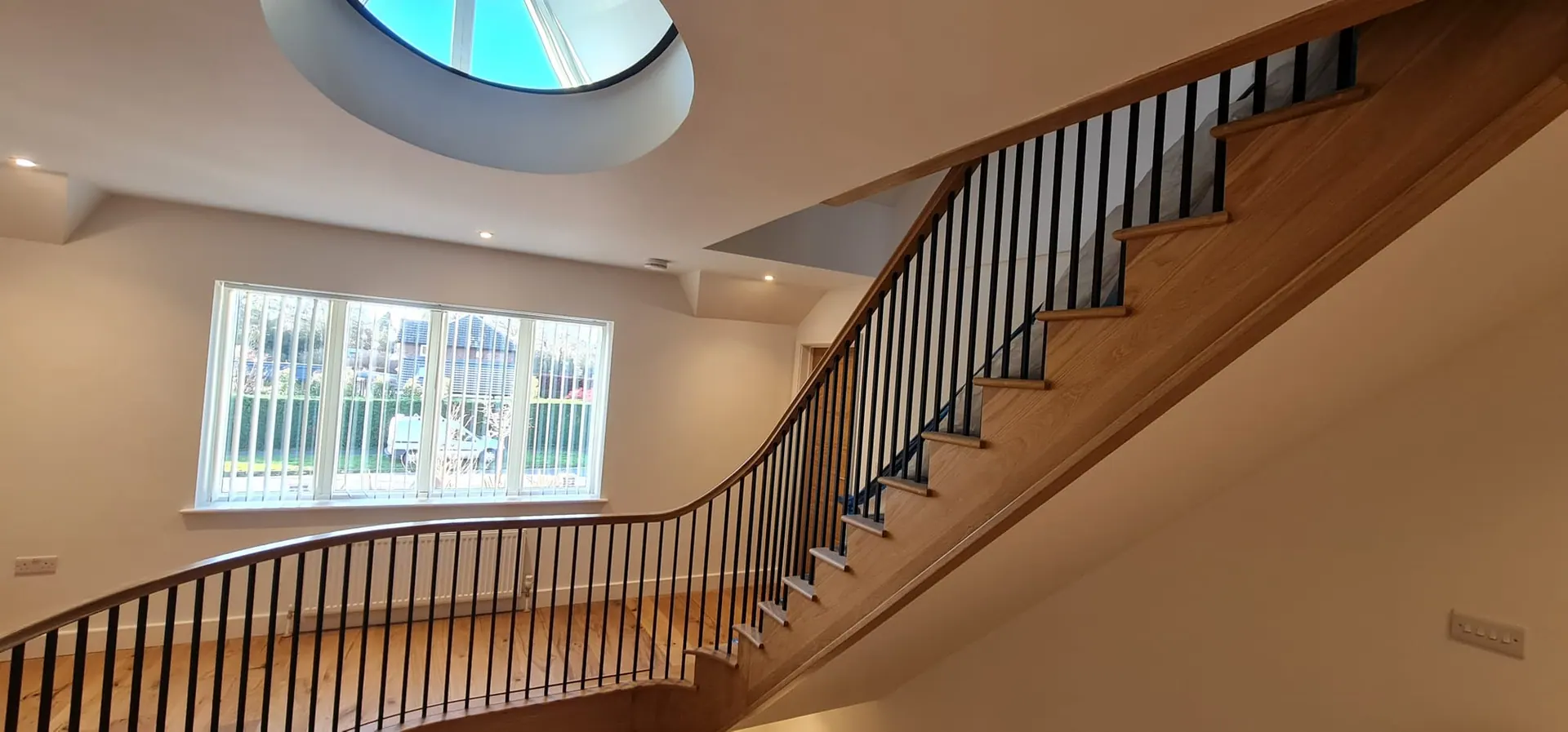 Curved oak staircase with black spindles below a round skylight